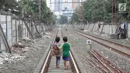 Dua anak berjalan usai bermain di sekitar rel kereta api di kawasan Pademangan, Jakarta, Kamis (8/11). Kurangnya lahan bermain menyebabkan anak-anak tersebut bermain di tempat yang tidak semestinya dan membahayakan. (Liputan6.com/Immanuel Antonius)