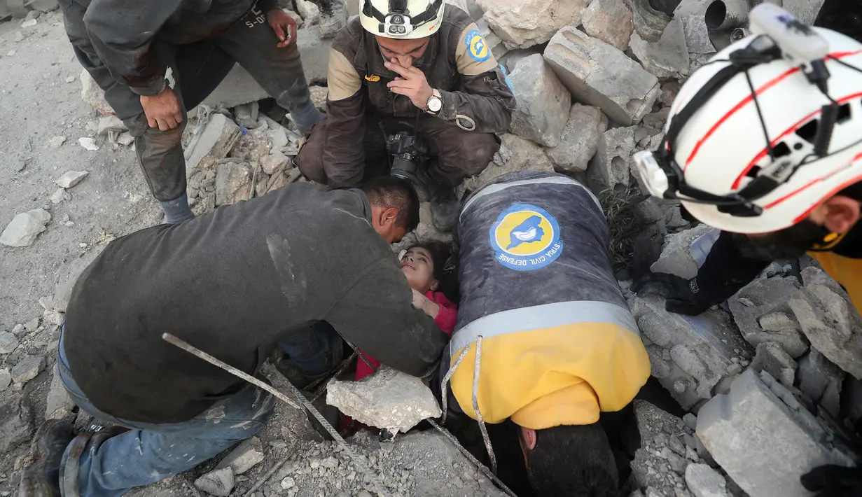 Anggota Syrian Civil Defence atau White Helmets berusaha menyelamatkan gadis yang tertimpa puing bangunan usai serangan udara pasukan pemerintah di Desa Tal Mardikh, Provinsi Idlib, Suriah, Kamis (19/12/2019). Pasukan Suriah kian intens menyerang Idlib. (Omar HAJ KADOUR/AFP)