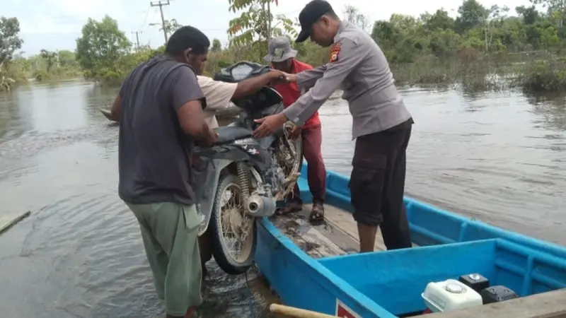 Personel Polsek Langgam jajaran Polres Pelalawan membantu mengangkat sepeda motor warga ke pompong untuk melintasi jalanan banjir.