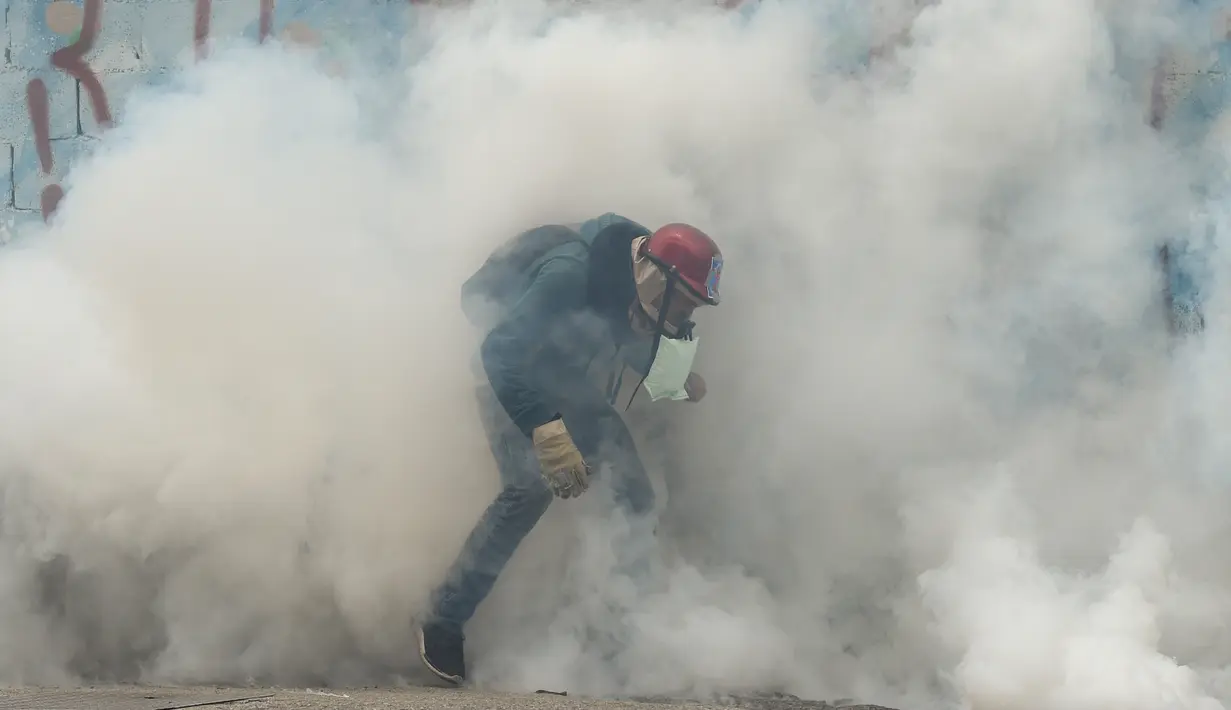 Asap gas air mata menyelimuti seorang demonstran saat aksi  menentang Presiden Venezuela Nicolas Maduro, di Caracas, kamis (20/4). Tiga orang dikabarkan tewas dalam aksi demonstrasi tersebut.  (AFP PHOTO / Juan BARRETO)