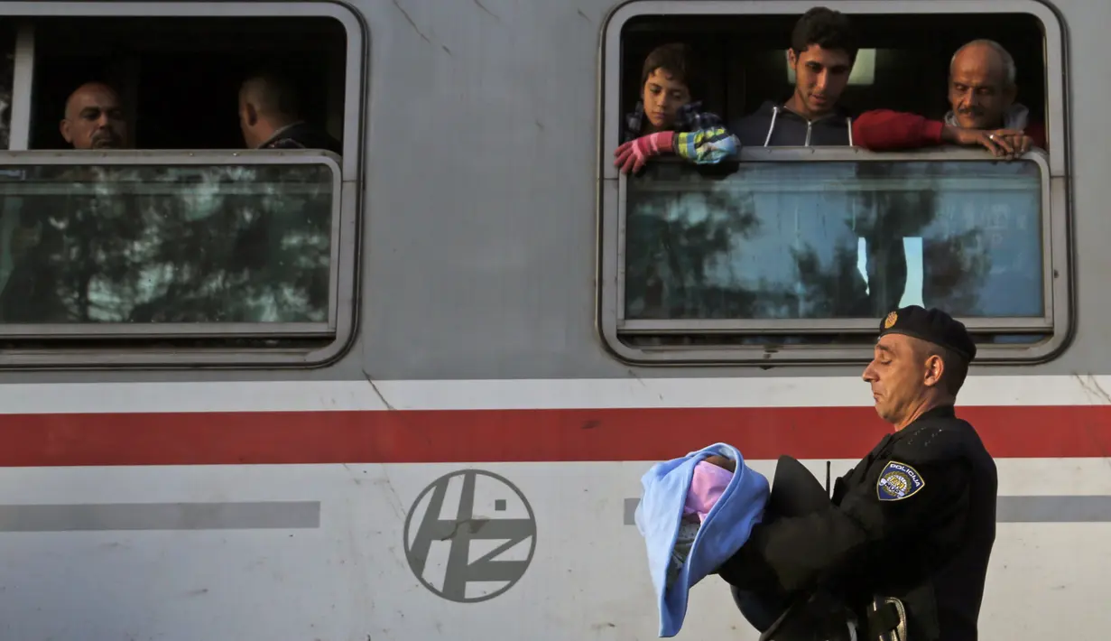 Seorang polisi menggendong seorang anak imigran saat yang akan naik kereta di stasiun kereta api di Tovarnik, Kroasia (21/9/2015). (REUTERS / Antonio Bronic)