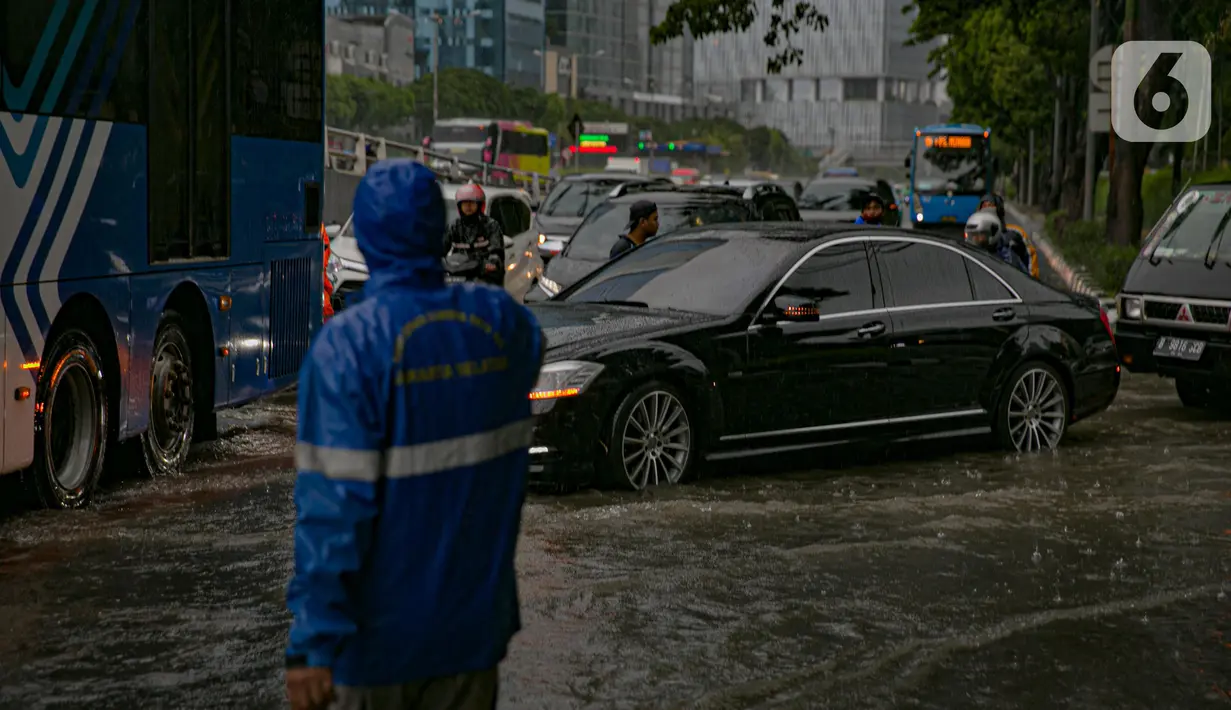 Petugas mengatur kelancaran lalu lintas saat air menggenangi ruas Jalan Gatot Subroto, Jakarta, Kamis (18/2/2021). Hujan deras yang mengguyur wilayah Jakarta menyebabkan terjadinya genangan di beberapa ruas jalan, meski begitu sejauh ini kendaraan masih dapat melintas. (Liputan6.com/Faizal Fanani)