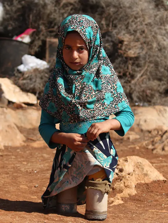 Maya Mohammad Ali Merhi (8) berjalan menggunakan kaki prostetik dari kaleng di sebuah kamp orang terlantar di Provinsi Idlib, Suriah, Rabu (20/6). Alat itu dipakai lantaran sang ayah tidak mampu membelikan kaki palsu yang sebenarnya. (Aaref Watad/AFP)