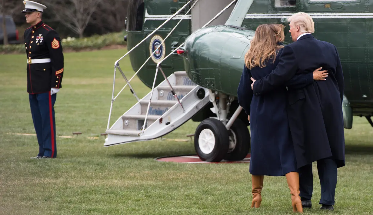 Presiden AS Donald Trump terlihat memegang ibu negara, Melania Trump yang hampir terjatuh saat berjalan menuju helikopter kepresidenan di halaman berumput Gedung Putih, Senin (19/3). Trump dan Melania hendak bertolak ke New Hempshire. (JIM WATSON/AFP)
