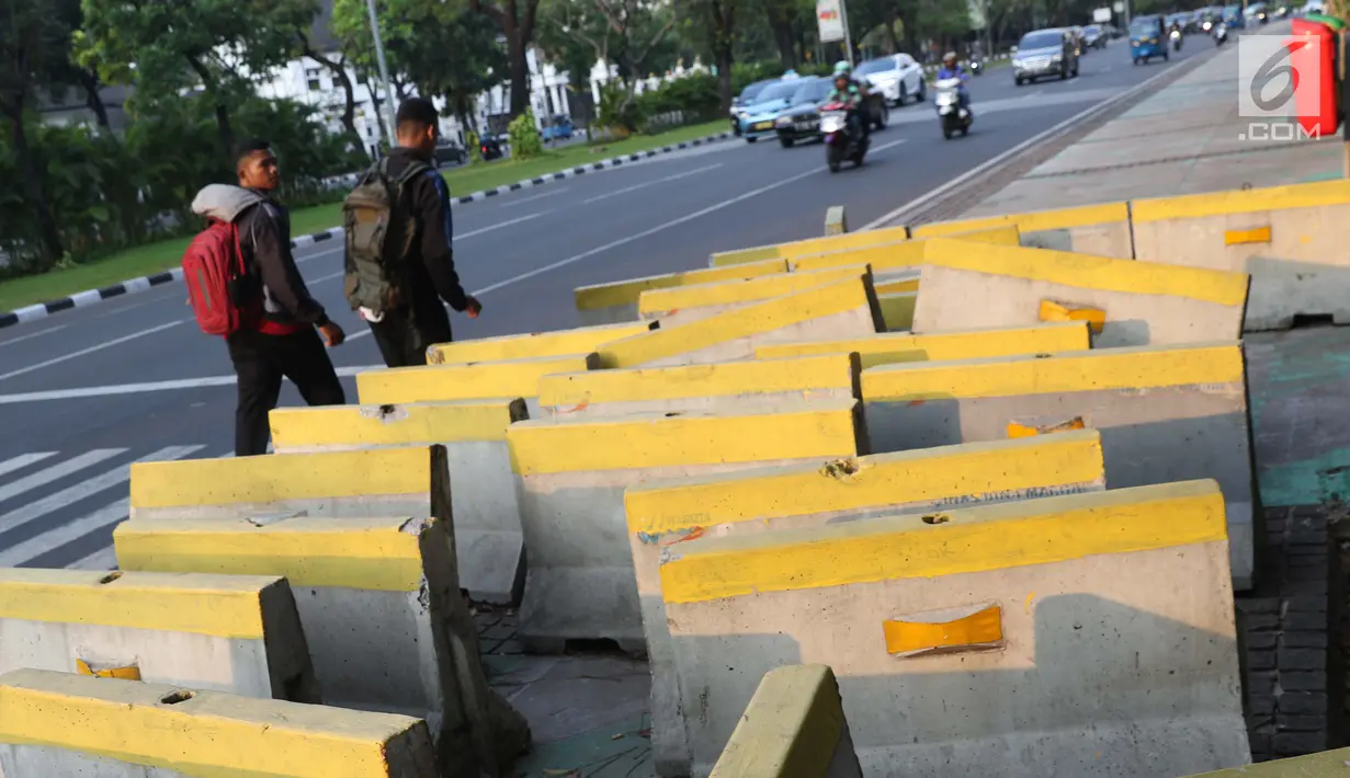 Pejalan kaki menghindari beton pembatas jalan yang diletakkan di atas trotoar Jalan Medan Merdeka Utara, Jakarta, Kamis (25/7/2019). Pembatas jalan yang berada tidak pada tempatnya mengganggu kenyamanan pejalan kaki yang melintasi trotoar jalan tersebut. (Liputan6.com/Helmi Fithriansyah)