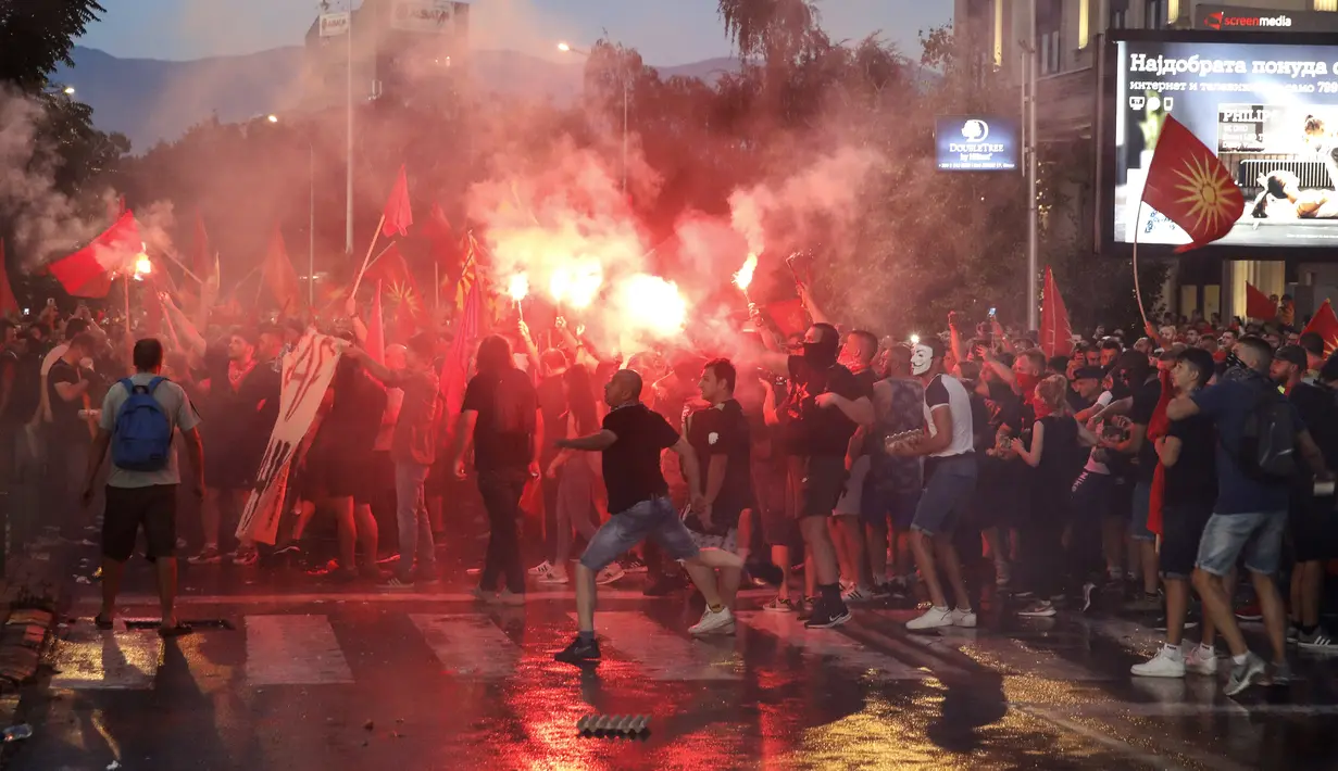 Orang-orang menyalakan suar dan melemparkan telur dan batu ke gedung kementerian luar negeri selama protes di Skopje, Makedonia Utara, Selasa (5/7/2022) malam. Protes kekerasan meletus di ibu kota Makedonia Utara, Skopje, di mana para demonstran mencoba menyerbu gedung-gedung pemerintah. (AP Photo/Boris Gdanoski)