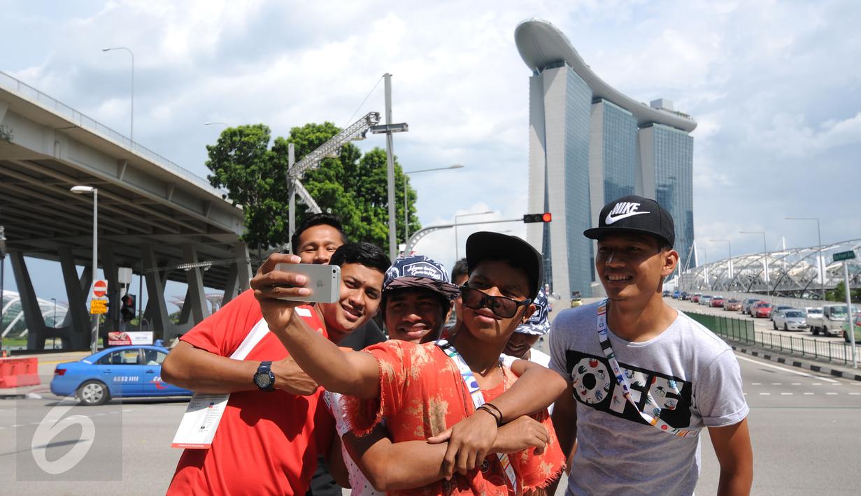 Para penggawa Garuda Muda bersantai sejenak usai melaksanakan ibadah salat Jumat di Masjid Sultan, Bugis, Singapura (5/6/2015). Manahati Lestusen (memegang ponsel) ber-selfie bersama rekannya di sekitar Merlion Park. (Liputan6.com/Helmi Fithriansyah)