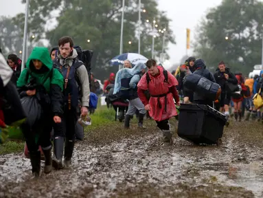 Penonton Festival Glastonbury tampak melewati jalanan yang banjir dan berlumpur saat tiba di Worthy Farm, Somerset, Inggris, (22/6). Festival Glastonbury merupakan festival musik paling populer di dunia. (REUTERS / Stoyan  Nenov)