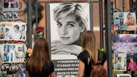 Dua wanita melihat potret Putri Diana dan kenangan lainnya yang dipajang di gerbang Istana Kensington, London, Selasa (30/8/2022). Minggu ini menandai peringatan 25 tahun kematian Putri Diana dalam kecelakaan mobil di Paris. (AP Photo/Alastair Grant)