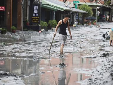 Seorang warga berjalan dengan sekop di sepanjang jalan yang tertutup lumpur di Hualien pada 24 September 2025, setelah bendungan danau jebol akibat terjangan Topan Super Ragasa. (I-Hwa Cheng/AFP)