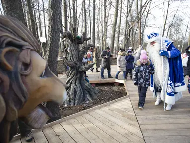 Seorang staf yang mengenakan kostum karakter dongeng Rusia, Kakek Frost, berjalan bersama anak-anak dalam pembukaan "Jalur Dongeng" di "Kediaman Kakek Frost" di Moskow, Rusia (18/11/2020). . (Xinhua/Alexander Zemlianichenko Jr)