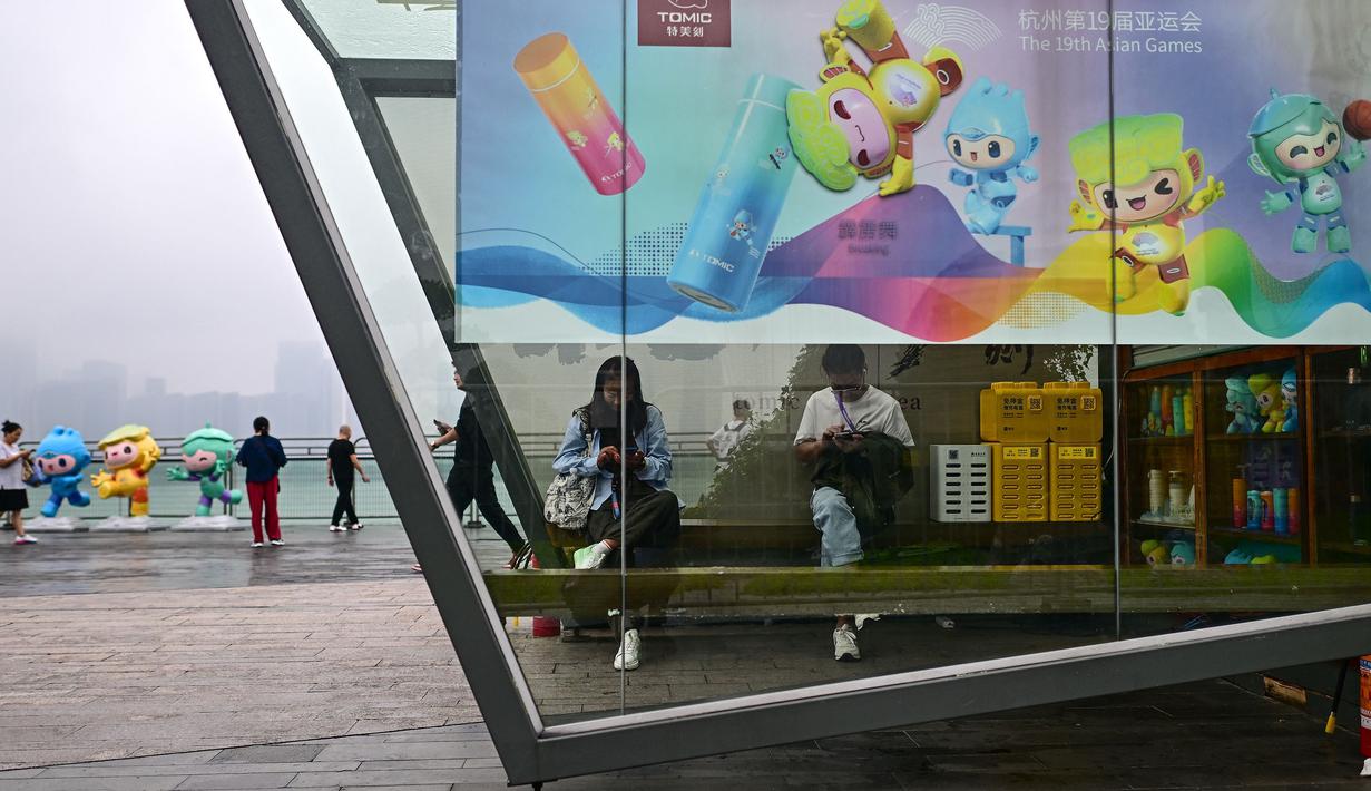 Sejumlah orang duduk di dalam stan yang dihiasi poster Asian Games 2022 di sepanjang kawasan pedestrian Sungai Qiantang di Hangzhou, Zhejiang,China pada 22 September 2023 waktu setempat. (AFP/Manan Vatsyayana)
