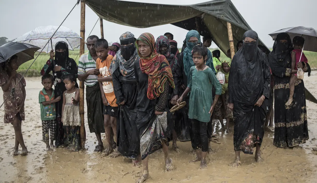 Pengungsi Muslim Rohingya menunggu antrean distribusi makanan di bawah tenda saat hujan di kamp pengungsi Nayapara, Bangladesh (6/10). Bangladesh akan membangun kamp pengungsi terbesar di dunia untuk menampung 800.000 orang. (AFP PHOTO/Fred Dufour)