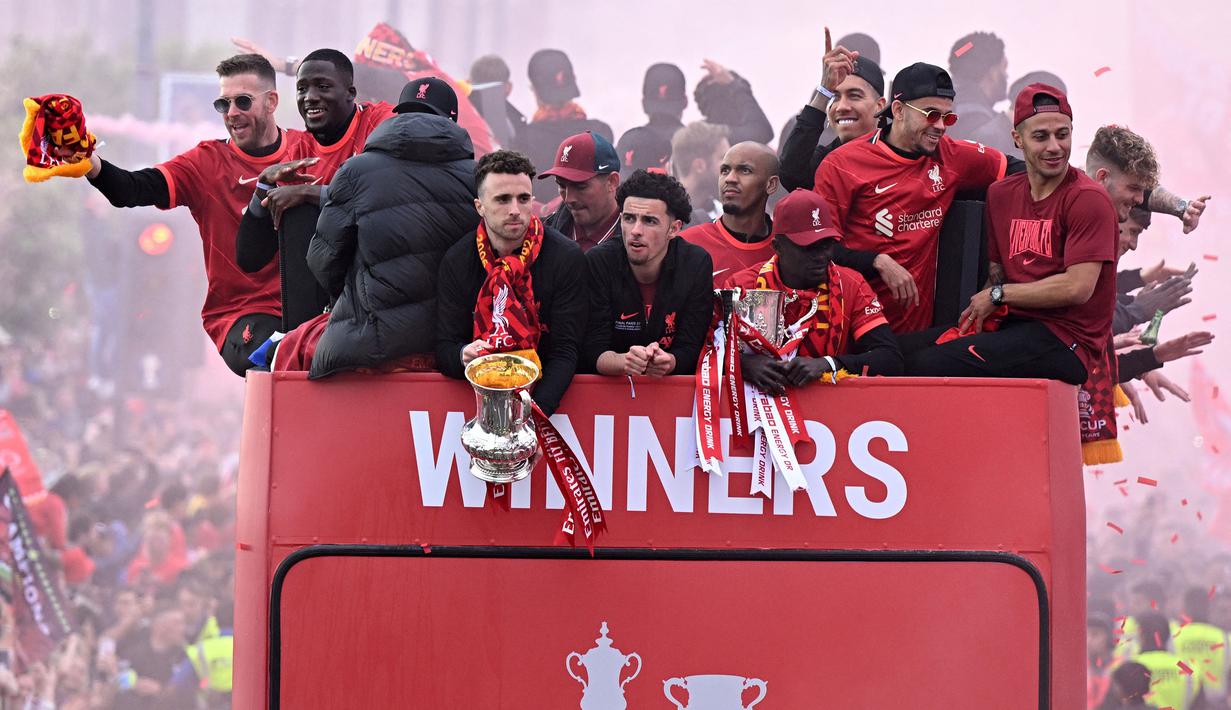 Para pemain Liverpool melambaikan tangan dan memegang dua trofi yaitu Piala FA dan Piala Liga Inggris di atas bus terbuka saat parade menyusuri jalan-jalan kota Liverpool pada Minggu (29/05/2022) waktu setempat. (AFP/Oli Scarff)