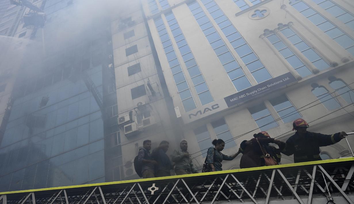 Petugas pemadam kebakaran Bangladesh menuntun orang menuruni tangga di bawah gedung kantor yang terbakar di Dhaka (28/3). Kebakaran besar melanda gedung perkantoran yang menewaskan sedikitnya lima orang dan lainnya masih terperangkap dalam gedung yang terbakar tersebut. (AFP/Munir Uzzaman)