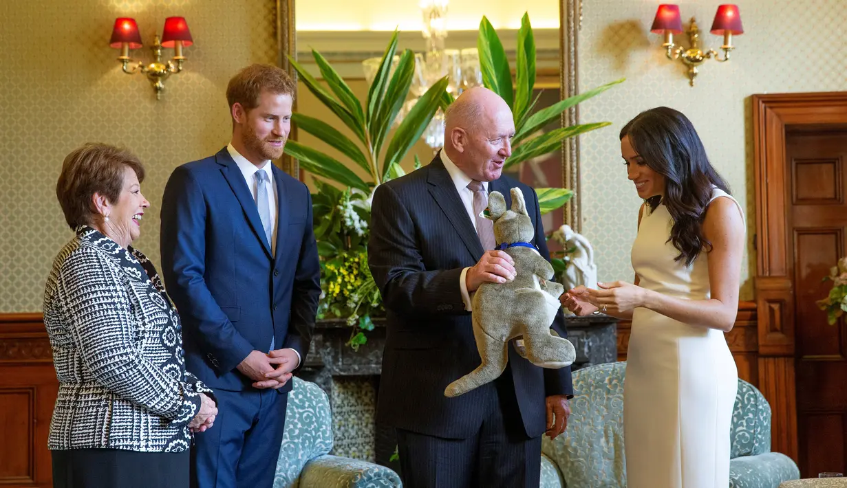Meghan Markle menerima hadiah boneka kangguru dari Gubernur Jenderal Australia Sir Peter Cosgrove dalam kunjungan resminya bersama Pangeran Harry di Sydney, Selasa (16/10). Meghan tampak senang menerima hadiah bayi pertamanya. (Steve Christo / POOL / AFP)