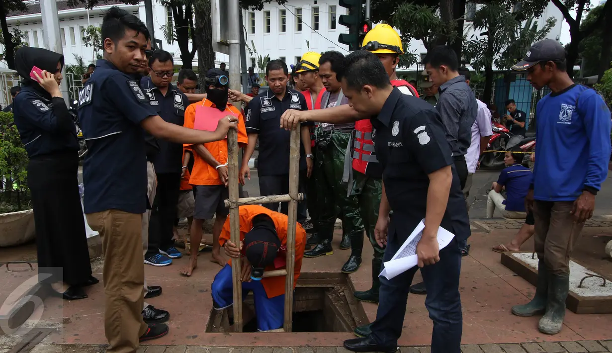 Para tersangka masuk ke dalam lubang gorong-gorong saat rekonstruksi pencurian kabel di Jalan Medan Merdeka Selatan, Jakarta, Selasa (15/3). 4 tersangka dihadirkan untuk menunjukkan cara mereka memotong dan mencuri kabel. (Liputan6.com/Immanuel Antonius)
