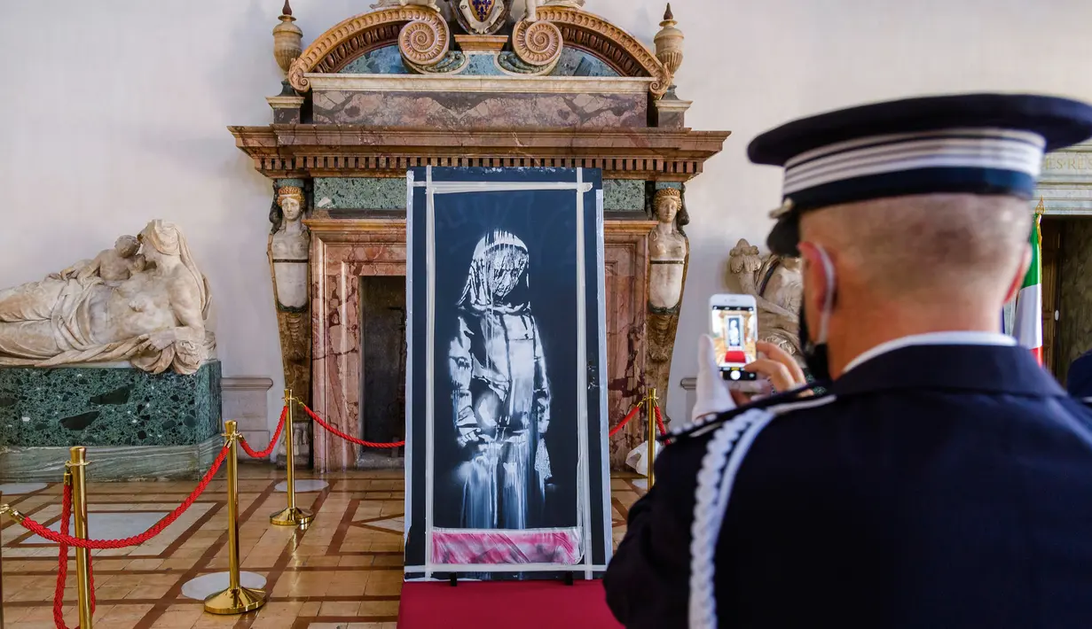 Seorang perwira Gendarmerie Prancis memfoto Lukisan seniman Inggris Banksy yang menggambarkan sosok perempuan muda dengan ekspresi sedih di Kedutaan Besar Prancis di Roma (14/7/2020). Karya seni itu dicuri pada 2018.  (AP/Photo/Domenico Stinellis)