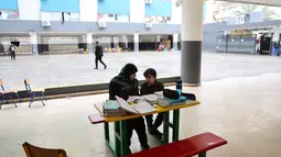 Eskalasi serangan udara Israel telah menyebabkan penutupan sekolah di Lebanon secara luas. Tampak dalam foto, seorang wanita Lebanon yang mengungsi duduk di samping seorang anak, mengawasi pelajaran daringnya melalui telepon seluler di sebuah sekolah negeri yang diubah menjadi tempat penampungan di kota Dekwaneh, utara Beirut, pada Rabu 25 Maret 2026. (Anwar AMRO/AFP)
