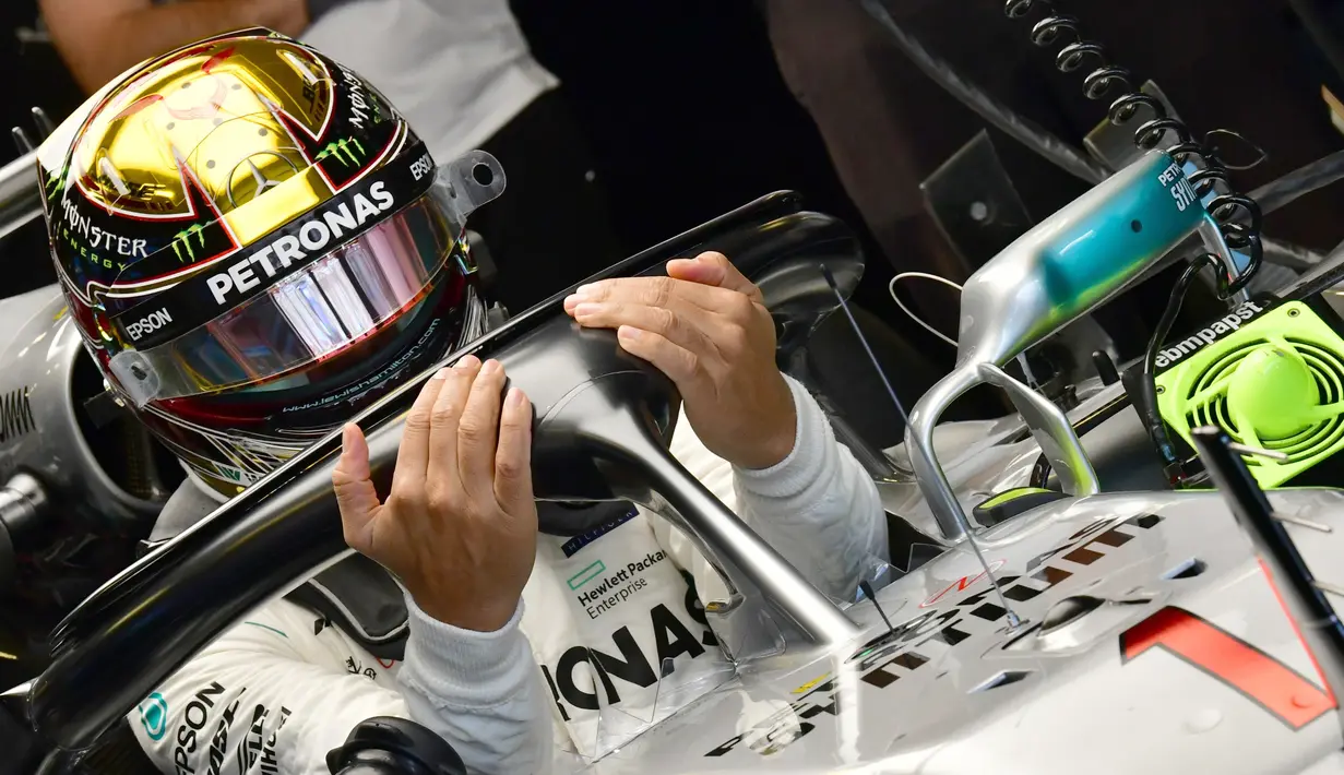 Pembalap Mercedes, Lewis Hamilton memasuki mobilnya saat sesi latihan pertama jelang GP F1 Abu Dhabi di Sirkuit Yas Marina, Jumat (23/11). Hamilton tampil berbeda dengan nomor balap yang melekat pada mobilnya. (GIUSEPPE CACACE/AFP)