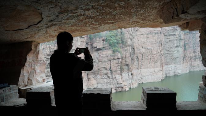 Seorang wisatawan memotret di jalur di tebing dekat Waduk Xiagou yang berada di Chaiguan, Kota Shahe, Provinsi Hebei, China utara, pada 28 Oktober 2020. Mengular berliku di sepanjang gunung, jalur tebing ini memiliki panjang 560 meter dan berada puluhan meter di atas permukaan air. (Xinhua/Mu Yu)