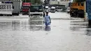 Hal ini dilakukan karena hujan lebat diperkirakan akan terjadi di negara gurun tersebut yang mengalami curah hujan rekor tahun lalu. Tampak dalam foto, seorang pria menerobos genangan air banjir setelah hujan lebat di Dubai, Uni Emirat Arab (UEA) pada Jumat 19 Desember 2025. (FADEL SENNA/AFP)