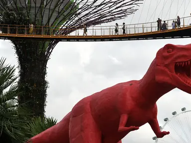 Pengunjung melihat patung dinosaurus di atas jembatan di Gardens by the Bay, Singapura, Senin (28/2). Rencananya akan dipamerkan sebanyak 11 dinosaurus beraneka warna untuk merayakan Festival Anak di Singapura. (AFP PHOTO / Roslan RAHMAN)