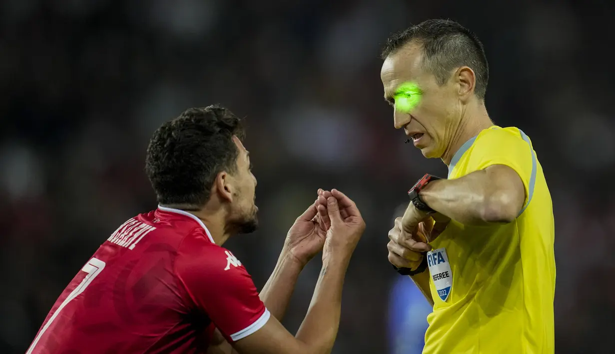 Wasit Ruddy Buquet memiliki sinar laser hijau yang diarahkan ke wajahnya saat berbicara dengan penyerang timnas Tunisia Youssef Msakni dalam laga uji coba internasional kontra Brasil di Stadion Parc des Princes, Rabu (28/9/2022) dini hari WIB. Timnas Brasil menang dengan skor telak 5-1 atas Tunisia dalam pertandingan FIFA Matchday. (AP Photo/Christophe Ena)