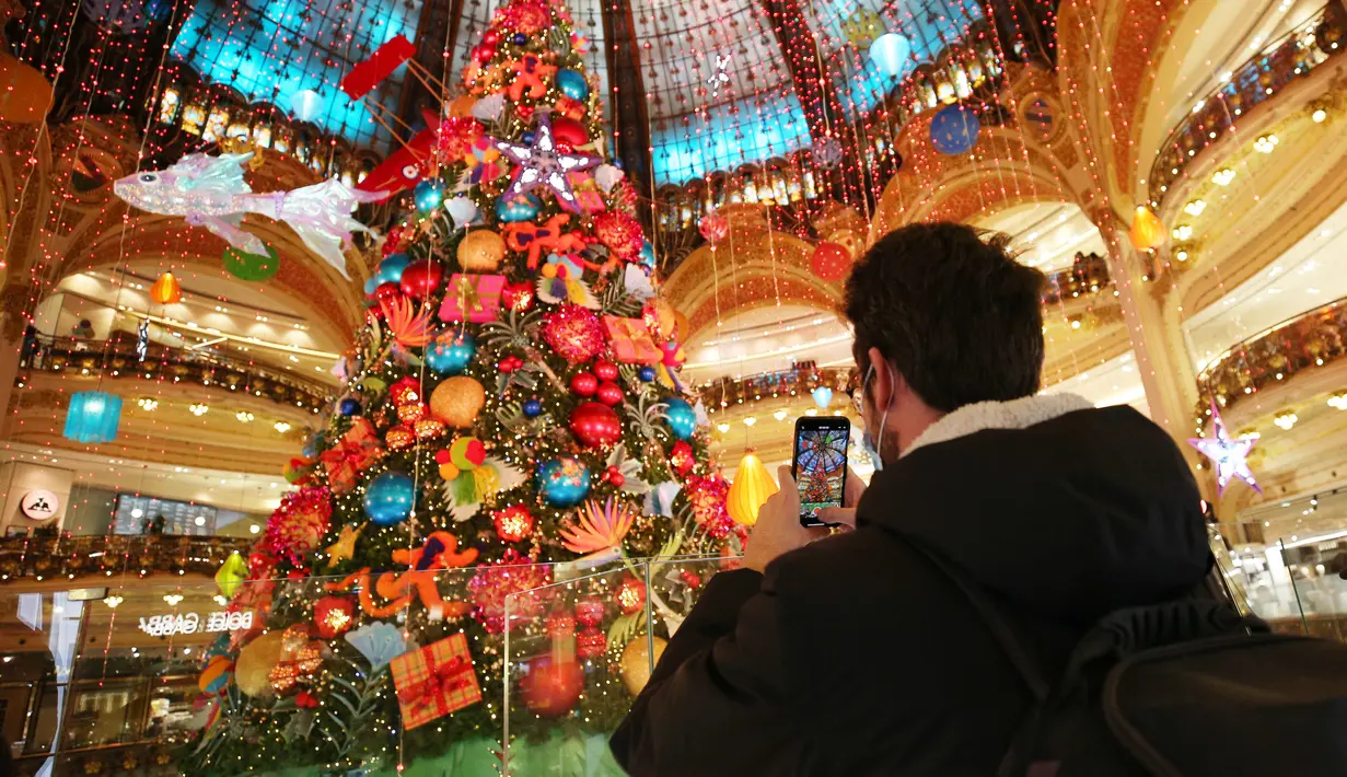 Seorang pria memotret pohon Natal raksasa di Lafayette saat hari pertama pembukaan kembali pusat perbelanjaan tersebut di Paris, Prancis, 28 November 2020. Prancis pada Sabtu (28/11) memulai tahap pertama dari tiga tahap strategi pelonggaran karantina wilayah (lockdown). (Xinhua/Gao Jing)
