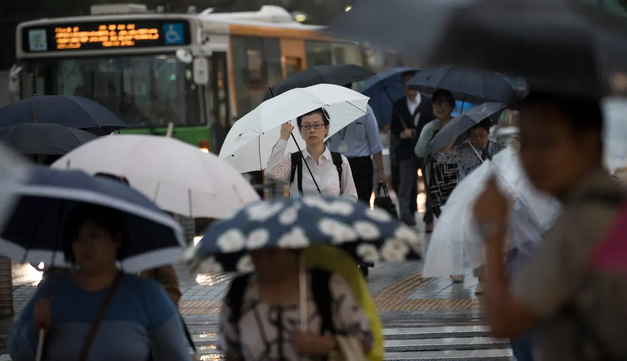 Pejalan kaki menggunakan payung berjalan saat hujan turun di Tokyo, Jepang (8/8). Sejumlah maskapai membatalkan penerbangan akibat cuaca yang kurang mendukung. (AFP Photo/Behrouz)