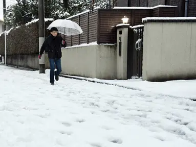 Seorang pria menggunakan payung berjalan di tumpukan salju yang menutupi jalanan di Tokyo, Jepang, Senin (18/1). Akibat banyaknya tumpukan salju yang menyelimuti daerah metropolitan Tokyo, moda transportasi massa pun lumpuh. (AFP PHOTO/Yoshikazu Tsuno)
