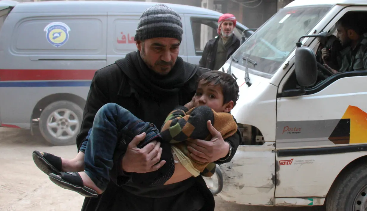 Seorang pria menggendong seorang anak untuk diselamatkan usai terjadi serangan udara dari pasukan Assad di wilayah Ghouta timur, Suriah (6/2). (AFP Photo/Hamza Al-Ajweh)