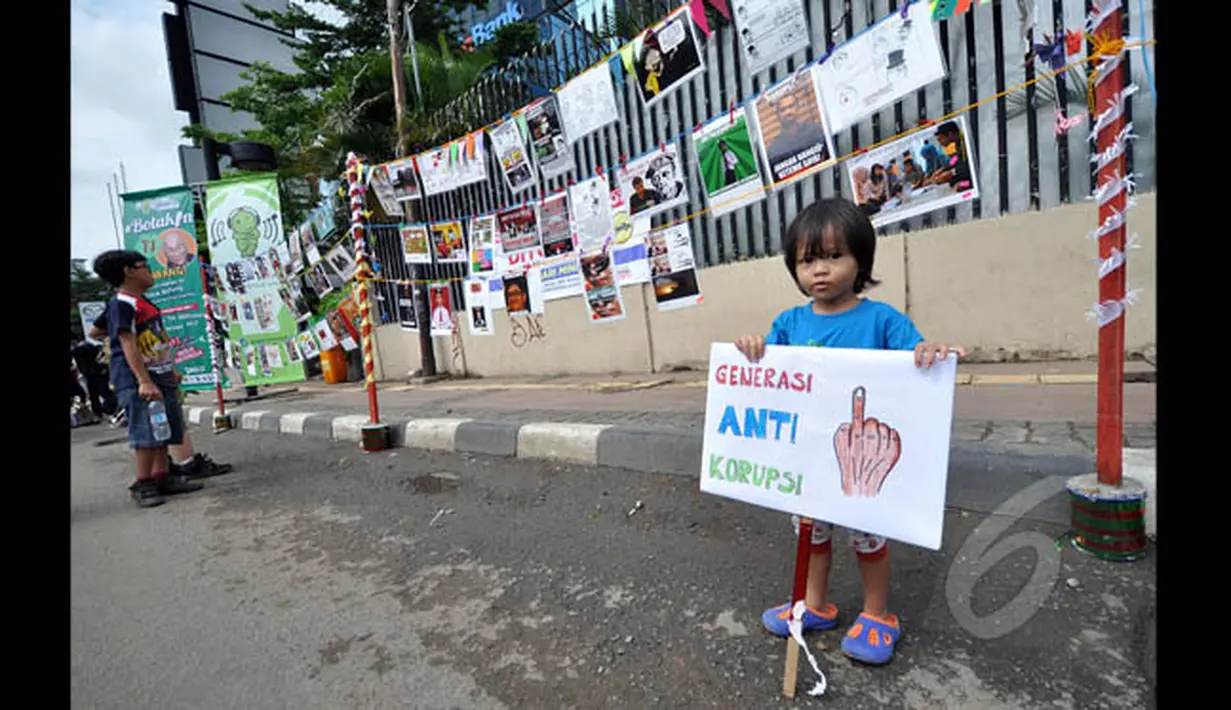 Seorang anak kecil tampak berdiri di depan pameran meme tentang korupsi yang digelar di Jalan MH Thamrin, Jakarta, Minggu (18/1/2015). (Liputan6.com/Miftahul Hayat)