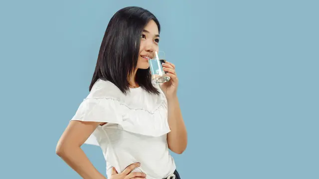 Seorang perempuan sedang berkacak pinggang sambil meminum segelas air (Foto Dok: Freepik/master1305)