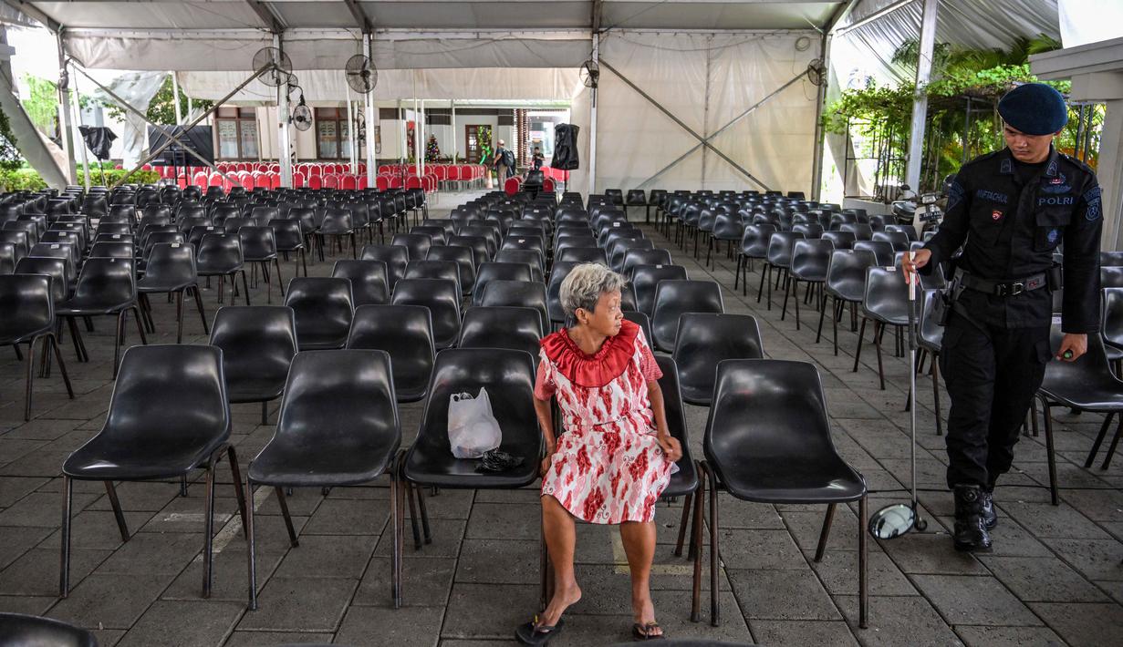 Tahun ini, Misa Natal mengangkat tema nasional, yakni "Allah Hadir Untuk Menyelamatkan Keluarga". Tampak dalam foto, seorang wanita lanjut usia memperhatikan salah satu personel dari unit Gegana dan Jihandak Brimob Polda Jawa Timur saat melakukan pemeriksaan di Gereja Katedral Hati Kudus Yesus, yang dikenal secara lokal sebagai gereja "Hati Kudus Yesus", Surabaya, pada Rabu 24 Desember 2025. (JUNI KRISWANTO/AFP)