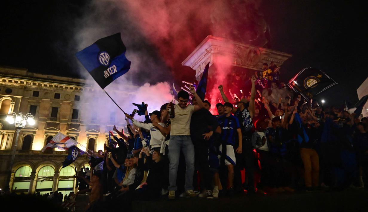 Di bawah guyuran hujan gerimis, pendukung Inter Milan tetap berkumpul hingga dini hari untuk menyalakan suar (flares) dan menyanyikan yel-yel kemenangan di bawah ikon katedral Duomo. Tampak dalam foto, para pendukung Inter Milan merayakan gelar juara Serie A musim 2025/2026 atau scudetto ke-21 di Piazza Duomo, Milan, Italia, Minggu (3/4/2026) malam waktu setempat atau Senin (4/5/2026) dini hari WIB. (PIERO CRUCIATTI/AFP)