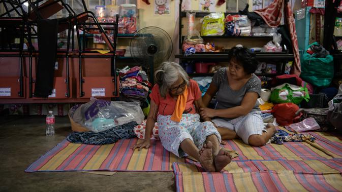 Wanita lanjut usia dibantu kerabatnya saat berada di pusat evakuasi korban letusan Gunung Taal di Sekolah Dasar Dona Tiburcia Carpio Malvar, Tanauan, Filipina, Rabu (16/1/2020). Pihak berwenang Filipina memperingatkan bahwa potensi Gunung Taal untuk kembali meletus masih tinggi. (Ed JONES/AFP)