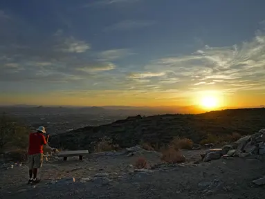 Seorang pejalan kaki memotret matahari terbit di atas Lembah di puncak South Mountain, Phoenix, Senin (17/7/2023). (AP Photo/Matt York)