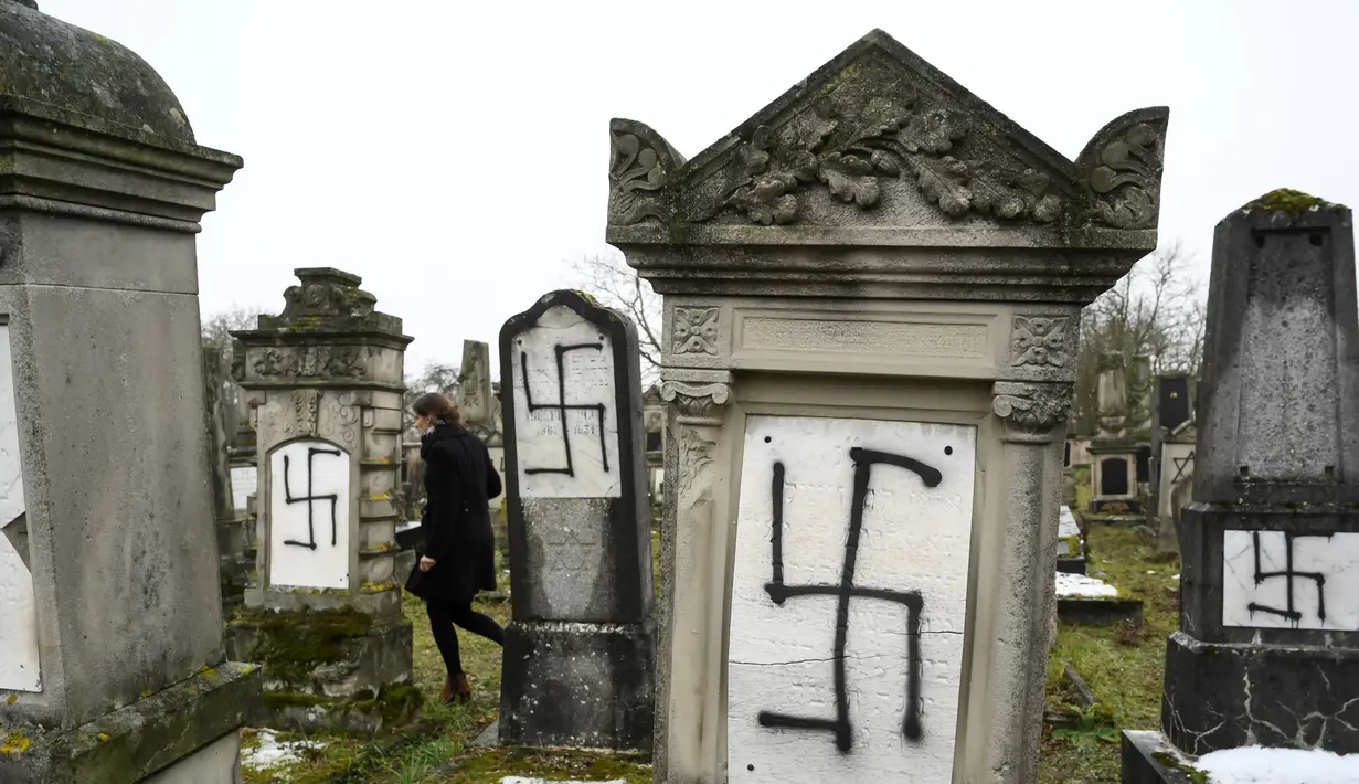 Seorang wanita berjalan di sebuah pemakaman Yahudi di Strasbourg, Prancis (17/12).  Sebanyak 37 batu nisan dirusak dengan lambang swastika Nazi yang dicat semprot dan grafiti lainnya. (AFP Photo/Sebastien Bozon)