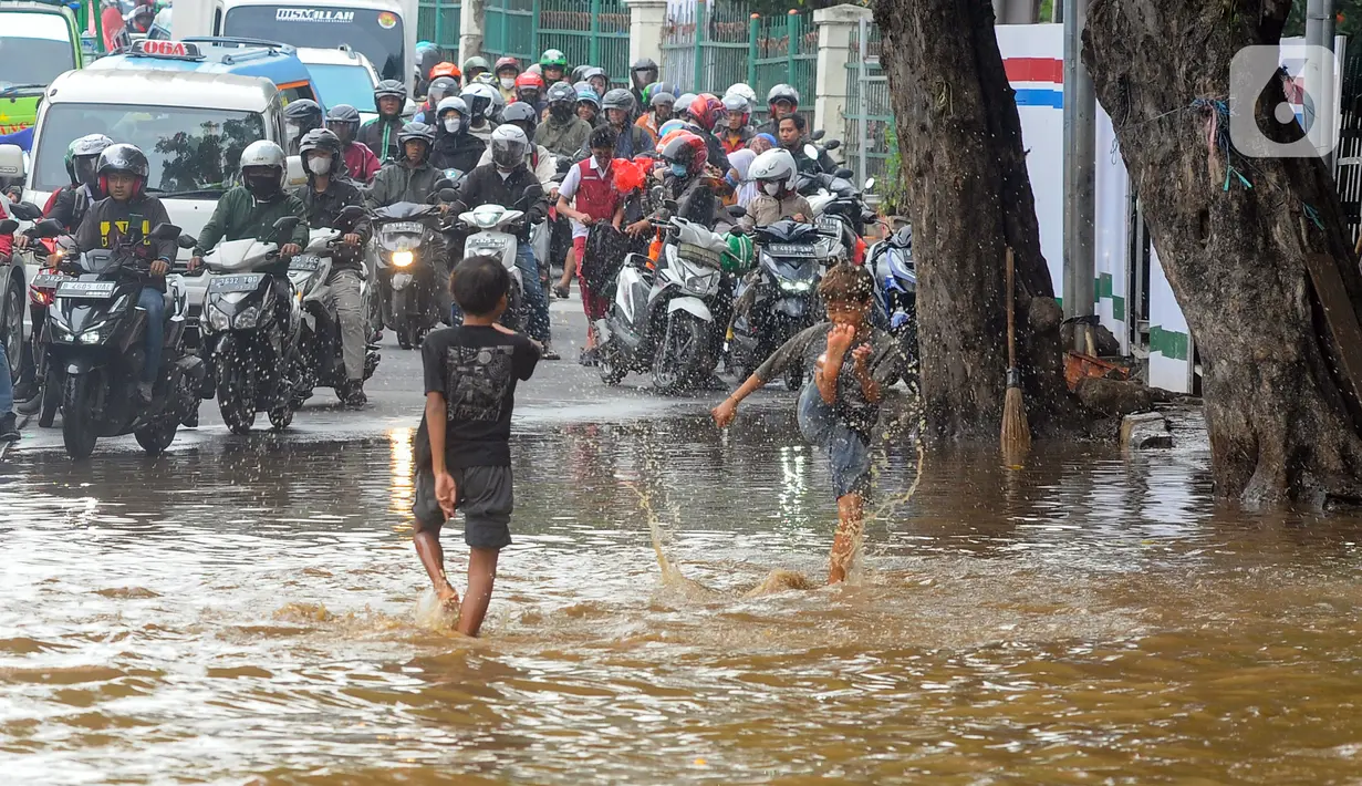 Anak-anak bermain air saat banjir meggenangi Jalan Raya Bogor di depan Pasar Induk Kramat Jati, Jakarta, Kamis (30/11/2023). (merdeka.com/Arie Basuki)