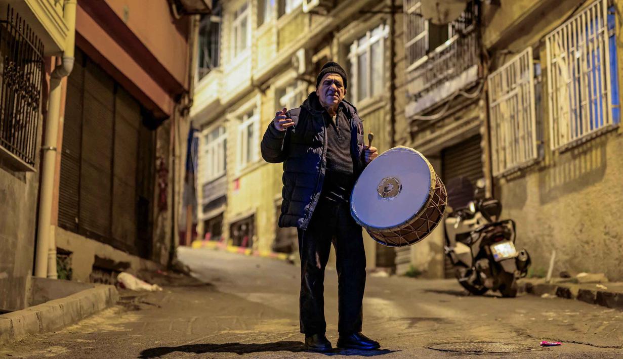 Penabuh gendang Turki, Hakan Ozbingol, memainkan gendang dan menyanyikan lagu-lagu tradisional di jalanan Istanbul, untuk membangunkan umat Muslim untuk sahur, yaitu makan malam Ramadan, pada 24 Februari 2026. Turki memiliki tradisi menabuh drum di jalan-jalan untuk membangunkan sahur sebelum memulai puasa di bulan suci Ramadan. (Yasin AKGUL/AFP)