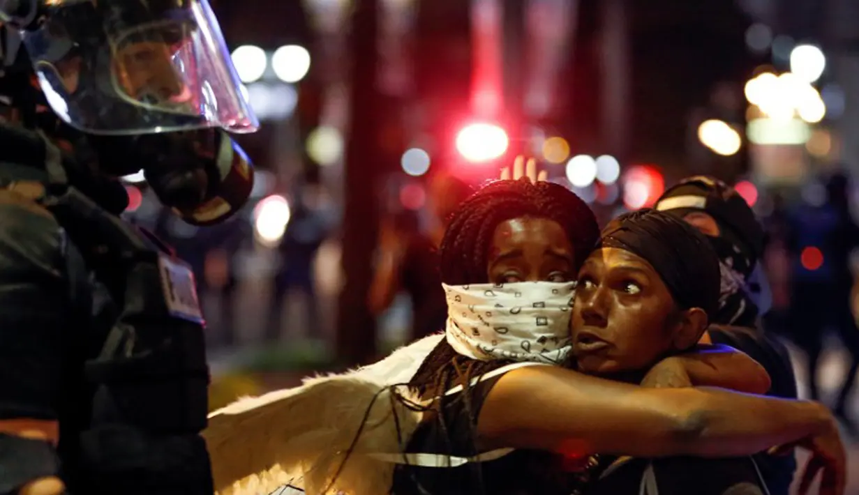 Dua orang pendemo menatap polisi yang berjaga di lokasi unjuk rasa di daerah Charlotte, North Carolina, AS, Rabu (21/9). Pengunjuk rasa protes atas penembakan pria kulit hitam oleh polisi. (REUTERS/Jason Miczek)