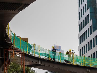 Pekerja menyelesaikan pengerjaan jembatan penyeberangan orang (JPO) dan jembatan penyeberangan sepeda di Karet Sudirman, Jakarta, Jumat (8/10/2021). JPO yang akan dilengkapi jalur sepeda dan terintegrasi dengan halte Transjakarta itu akan rampung pada November 2021. (Liputan6.com/Johan Tallo)