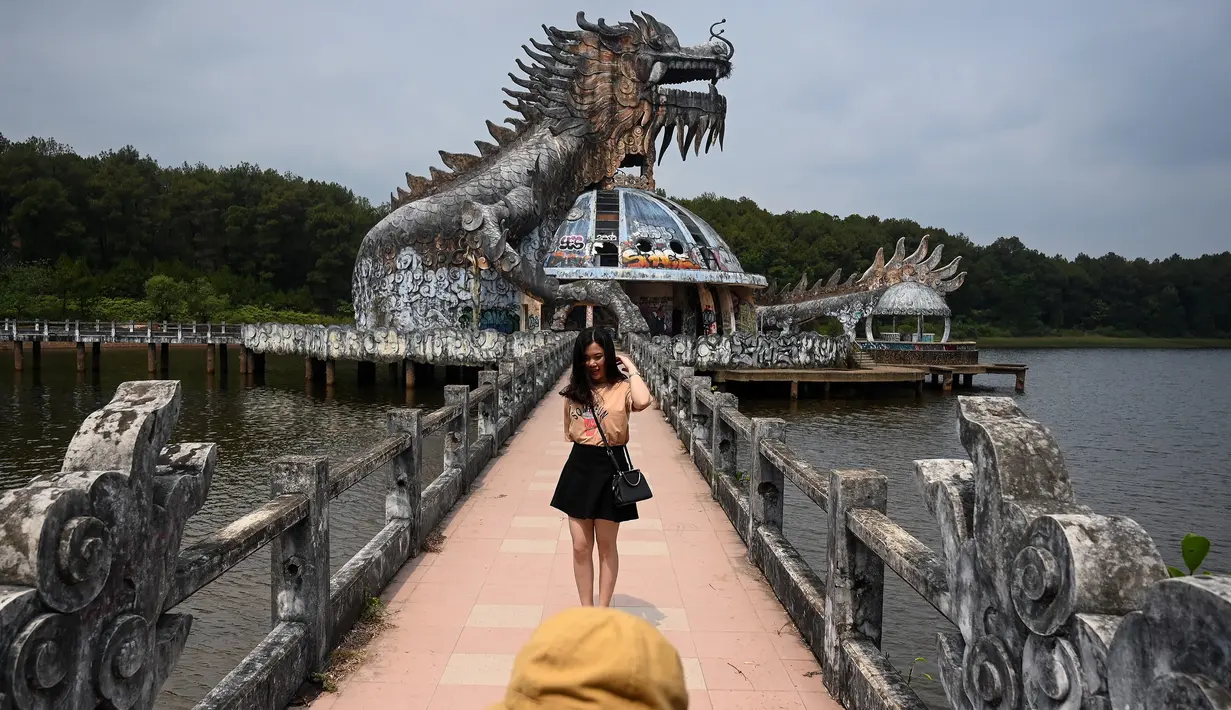 Foto pada 27 April 2019 memperlihatkan pengunjung berpose di depan bangunan berbentuk naga di Taman Air Ho Thuy Tien yang telah lama ditinggalkan di kota Hue, Vietnam. Taman air Ho Thuy Tien pertama kali dibuka untuk umum dalam keadaan setengah selesai pada tahun 2004. (Manan VATSYAYANA/AFP)