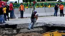 Petugas menggunakan derek turun ke dasar sebuah lubang yang tiba-tiba muncul di jalan raya Meksiko-Cuenava, Meksiko, Rabu (12/7). Lubang tersebut menelan seorang ayah dan putranya yang tengah berkendara dengan mobil. (AP/Tony Rivera)