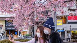 Orang-orang berfoto dengan bunga sakura di Taman Ueno di Tokyo, Jepang, Senin (21/3/2022). Suhu tinggi sejak awal Maret mungkin menyebabkan musim mekarnya sakura lebih cepat dibandingkan biasanya. (Philip FONG / AFP)