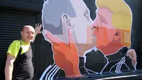 Warga berpose disamping mural calon Presiden AS, Donald Trump dan Presiden Rusia, Vladimir Putin sedang berciuman di Vilnius , Lithuania, (13/5). Hal ini diperkuat dengan pernyataan Trump bahwa Putin adalah pemimpin yang kuat. (AFP PHOTO/Petras Malukas)