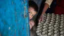 Seorang anak melihat keluar pintu ketika pengrajin tembikar membawa lampu minyak yang terbuat dari tanah liat untuk dikeringkan menjelang festival Diwali di Prayagraj, India, Kamis (17/10/2019).  Diwali merupakan festival lampu yang penting bagi umat Hindu di seluruh dunia. (AP/Rajesh Kumar Singh)