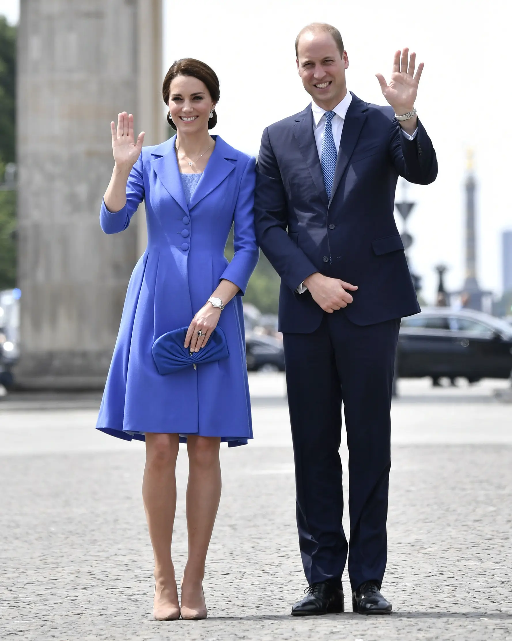 Pangeran William dan Kate Middleton melambaikan tangan sambil berpose di depan Gerbang Brandenburg di Berlin, Rabu (19/7). Pangeran William terlihat mengenakan setelan biru navy model klasik dan dasi biru untuk mengimbangi sang istri (John MACDOUGALL/AFP)