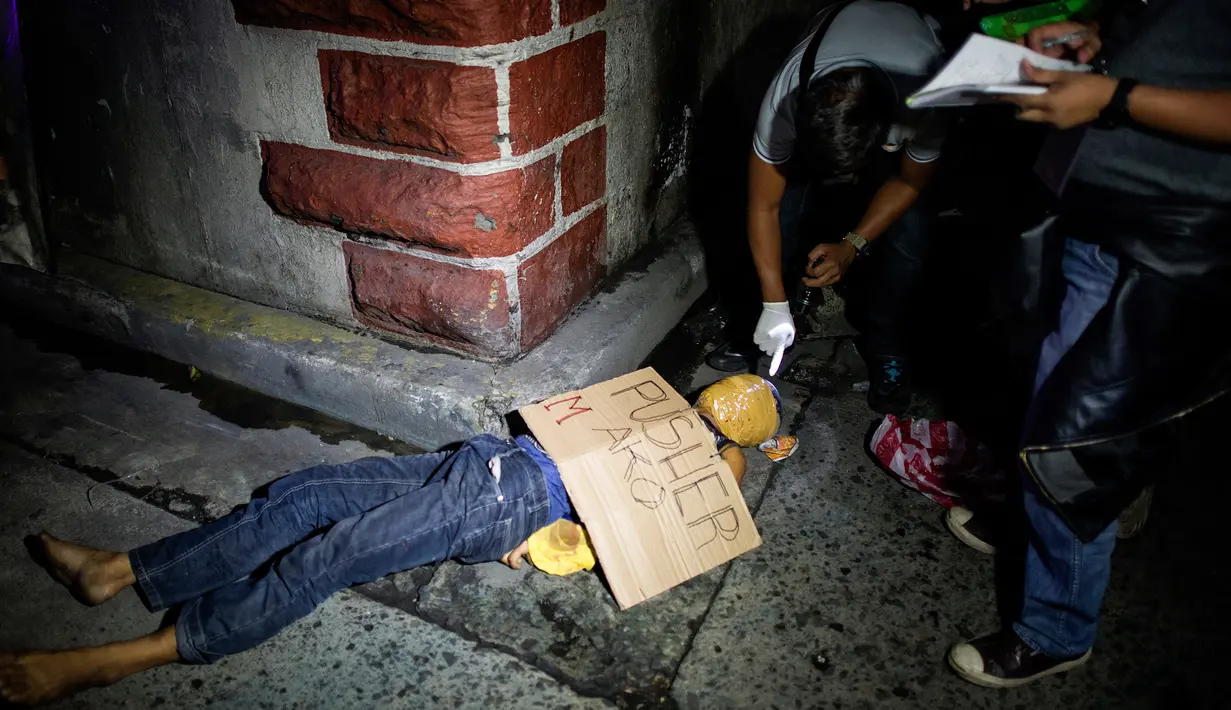Gambar yang diambil pada 8 Juli 2016 memperlihatkan petugas kepolisian Filipina memeriksa mayat yang diduga seorang pengedar narkoba dengan kondisi kepala terbungkus lakban di sebuah jalan di Manila. (AFP PHOTO/Noel CELIS)